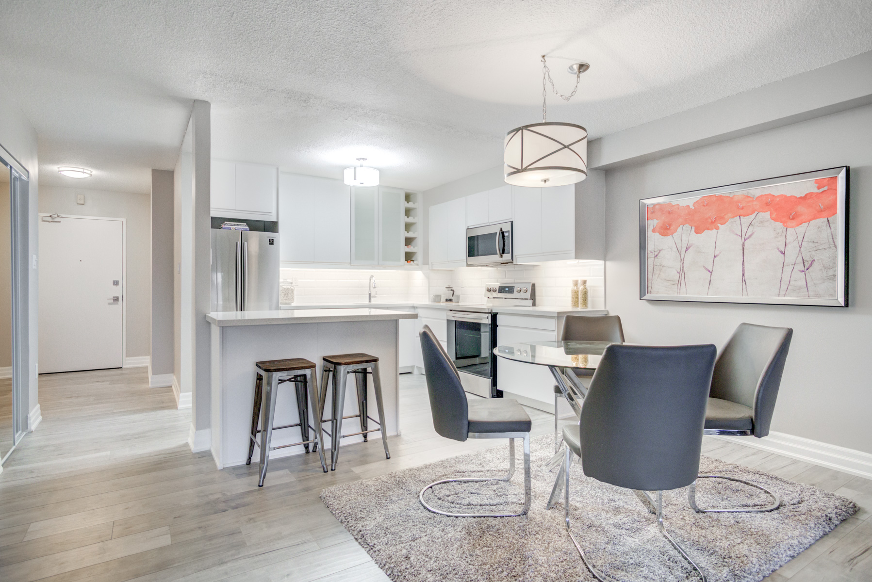 Interior image of a condominium showcasing a beautiful white kitchen with stainless steel appliances