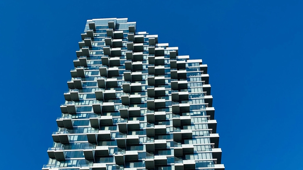 An image of a tall building which has condo maintenance fees towers over the photographer against a dark blue sky.