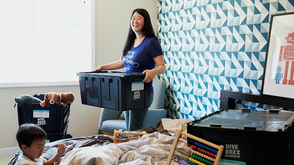 An image of a tenant - who is a mother with her son playing on the bed - moving and unpacking her belongings in their new bedroom.