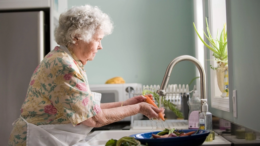 An image of a senior, elderly lady cooking at home in her new place after she downsized for retirement.