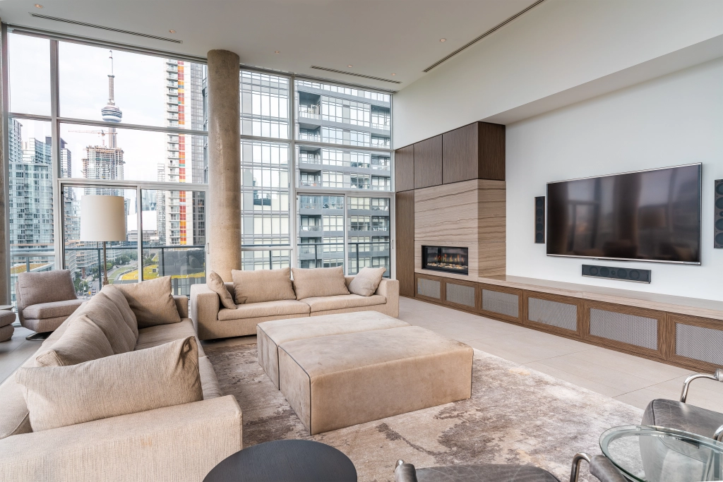 Interior image of 169 Fort York Blvd's upper penthouse showing the living room with the floor to ceiling windows open in the background with the CN tower in sight.