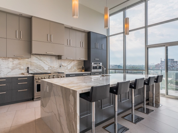 Interior image of 169 Fort York Blvd's upper penthouse showing the kitchen island and floor to ceiling windows open in the background facing north west