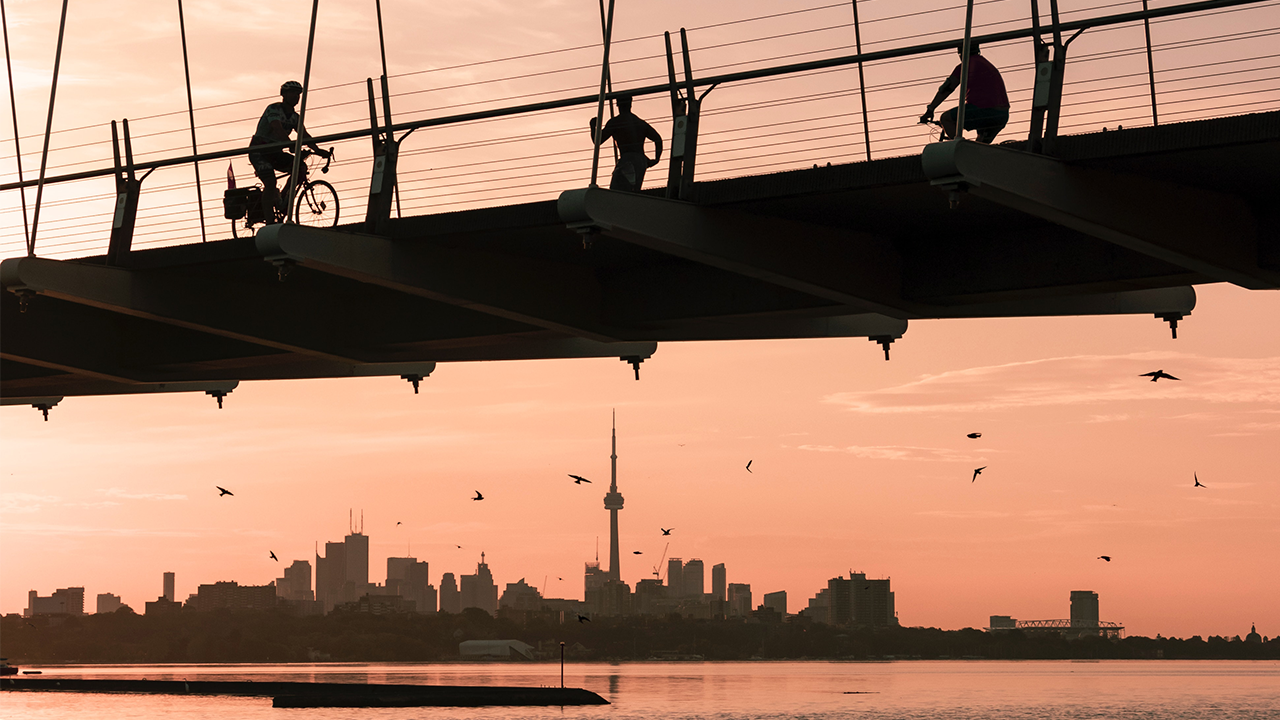 An image depicting one of the reasons why you might want to move to Etobicoke - the unique architecture of the Humber Bay Bridge with the iconic CN Tower behind it during a golden sunset.