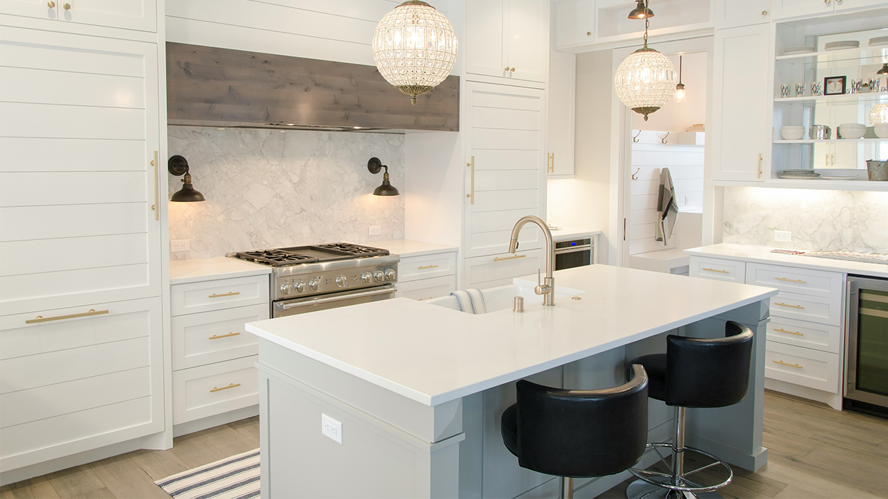An image of a modern, luxury kitchen with a waterfall kitchen island and white tiles.