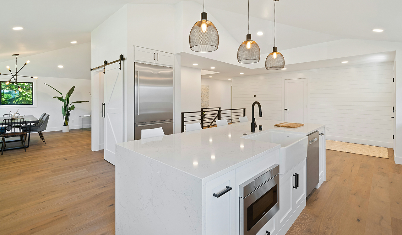 An image of a beautiful, farm-house style kitchen with white counter tops and wooden floor.