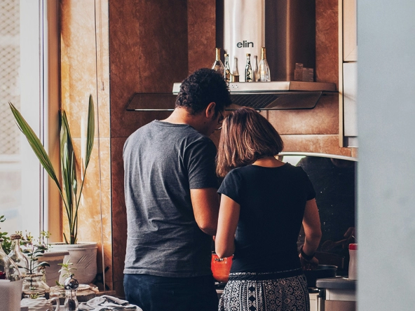 An image of a couple cooking in a kitchen with their back towards the camera.