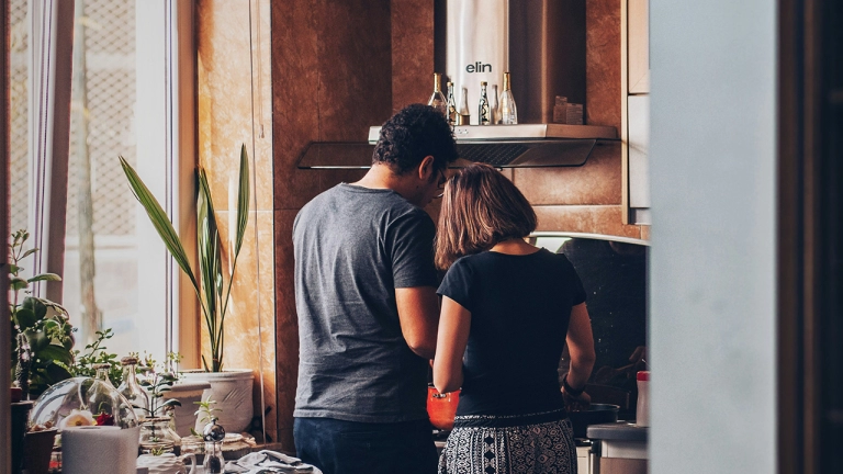 An image of a couple cooking in a kitchen with their back towards the camera.